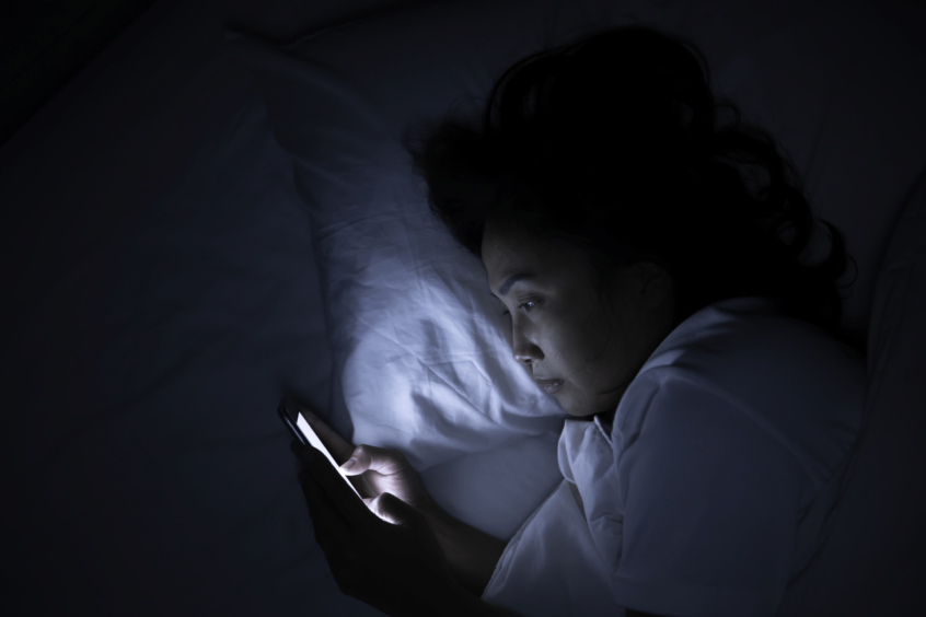 Image of person laying in bed looking at their smartphone